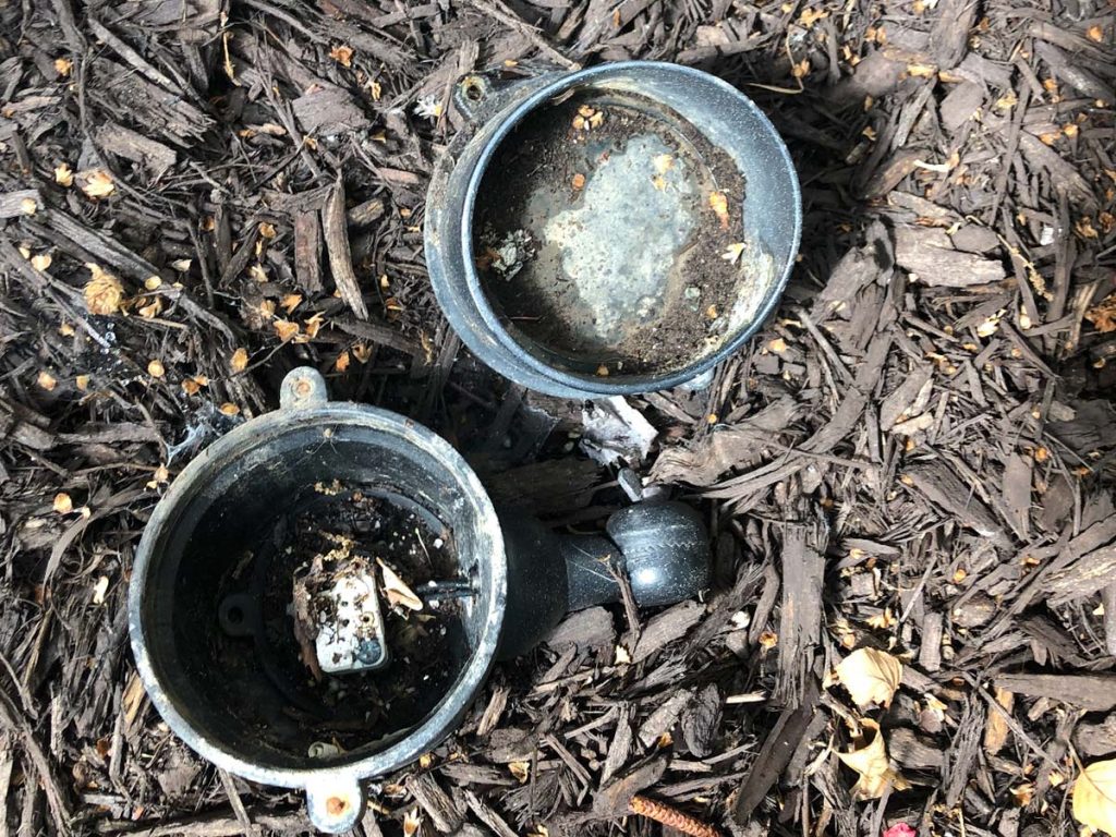 Two black, circular light fixtures are shown disassembled and resting on brown wood mulch.