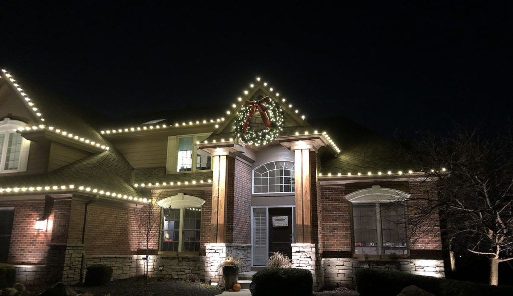 A brick home features glowing trim across roof peaks and eaves, demonstrating how Permanent Roofline Lighting enhances nighttime curb appeal.