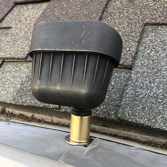 Robust bronze gutter light fixture is mounted securely onto a gutter system protected by a mesh leaf guard. Professional installation provides targeted illumination for upper rooflines or gabled areas on residential properties.
