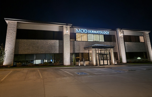 This two-story commercial building for "MOD DERMATOLOGY" is illuminated by bright exterior accent lighting on its textured brick pillars.
