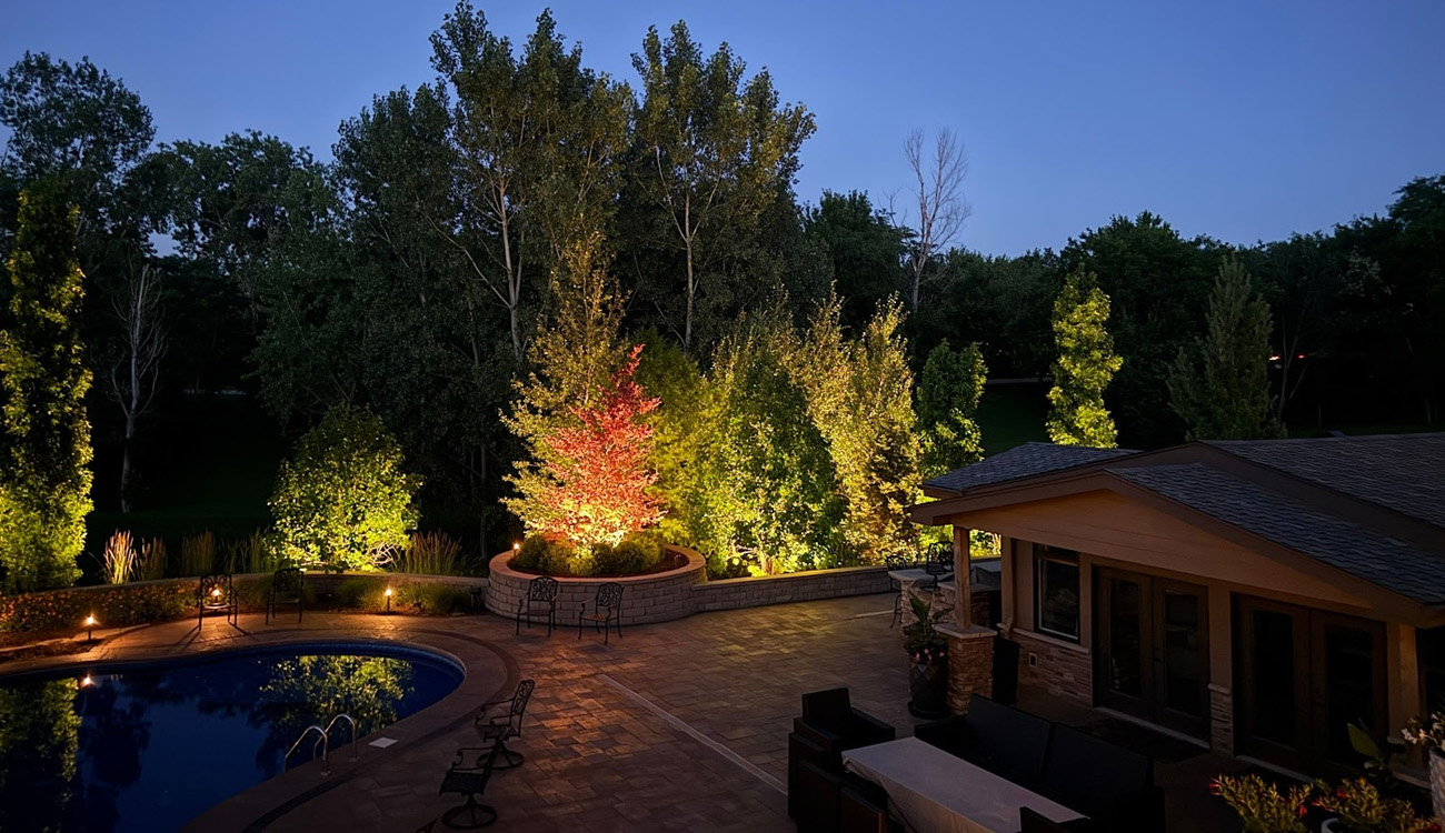 Illuminated backyard with pool and trees.