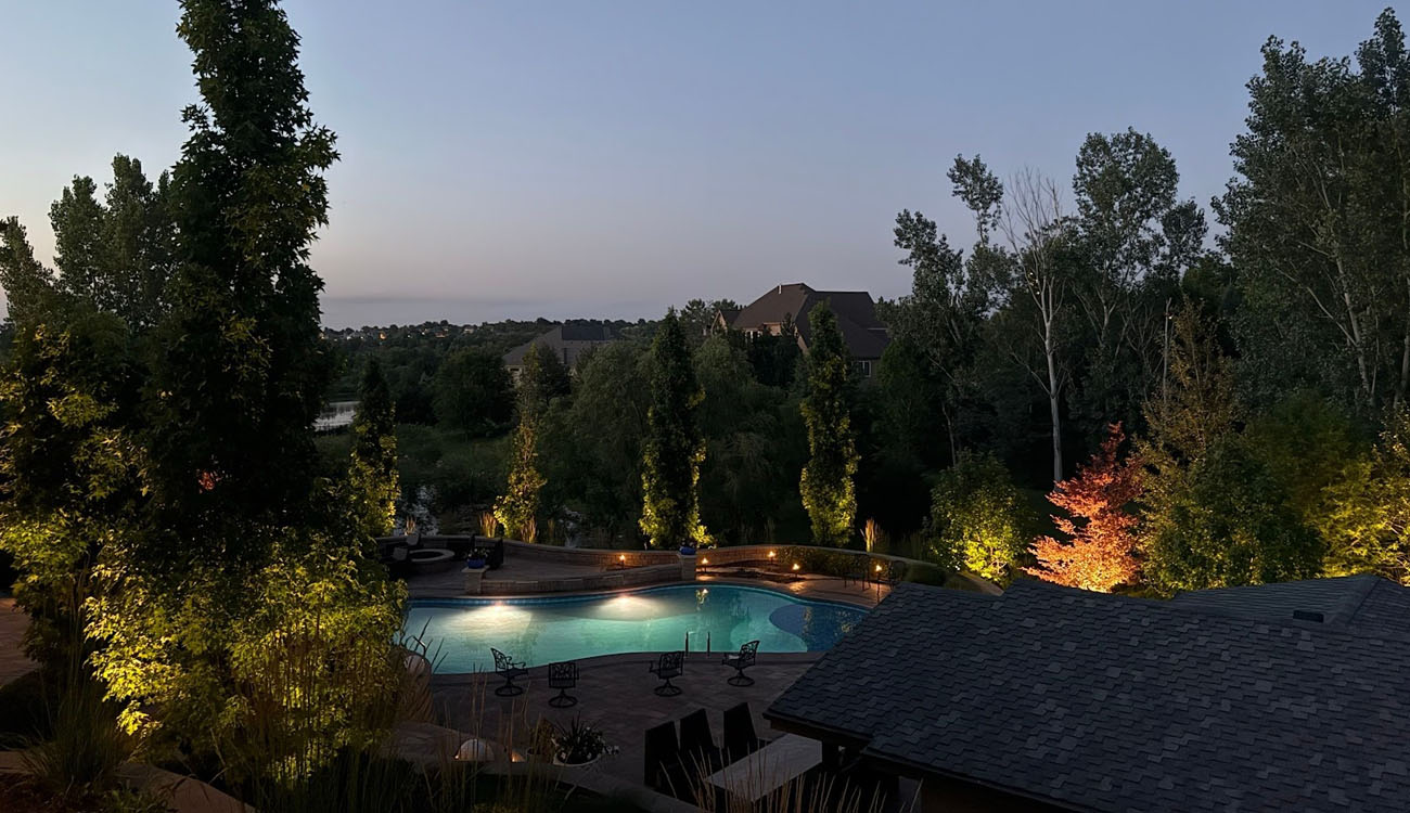 Residential pool and backyard highlighted with elegant landscape lighting design for trees and pathways in Omaha, Nebraska.