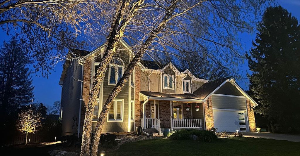 Residential home at night illuminated by professional outdoor lighting maintenance showcasing tree and façade lighting.