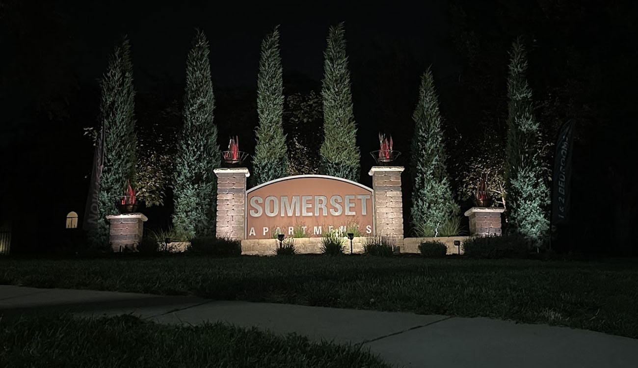 Multi-pillar apartment entry sign illuminated by commercial outdoor lighting solutions for enhanced nighttime visibility.