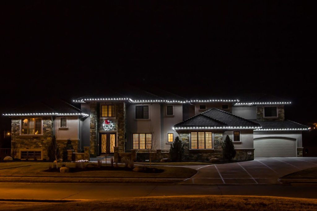 A large two-story home glows with bright trim lights along the roof, showing how Permanent Roofline Lighting adds year-round visibility and style.
