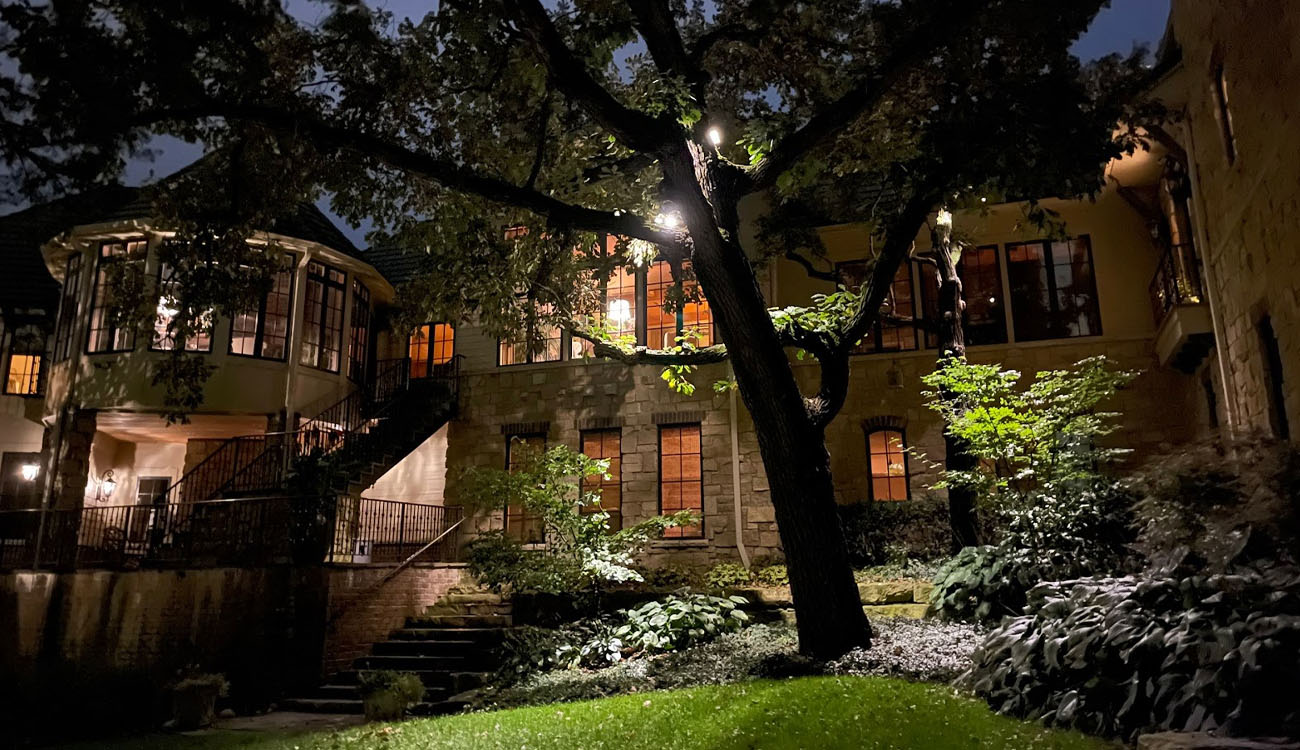 Strategic lights illuminate a grand stone estate, casting soft glows on lush trees and stairways.