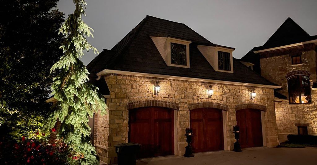 A wide view of a lit driveway and garden, featuring glowing trees and path illumination.