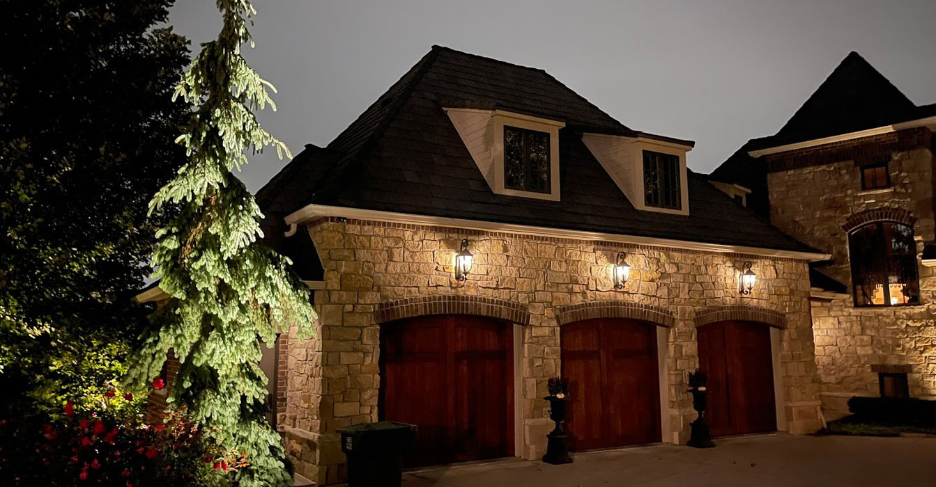 A wide view of a lit driveway and garden, featuring glowing trees and path illumination.