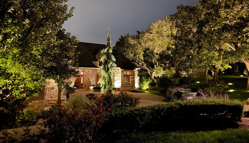 Warm lanterns highlight the textures of a stone garage, complemented by bright, evergreen focal lighting.