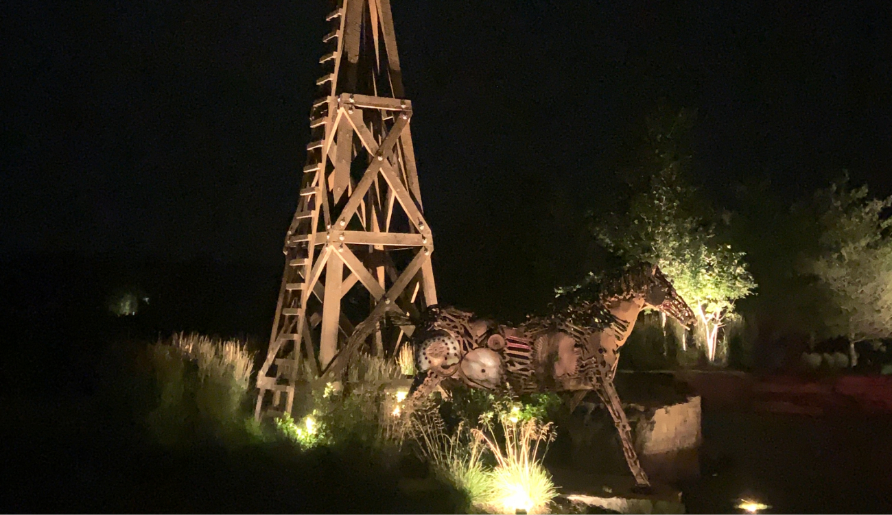 A wooden windmill and metal horse sculpture illuminated at night, demonstrating creative landscape lighting services.