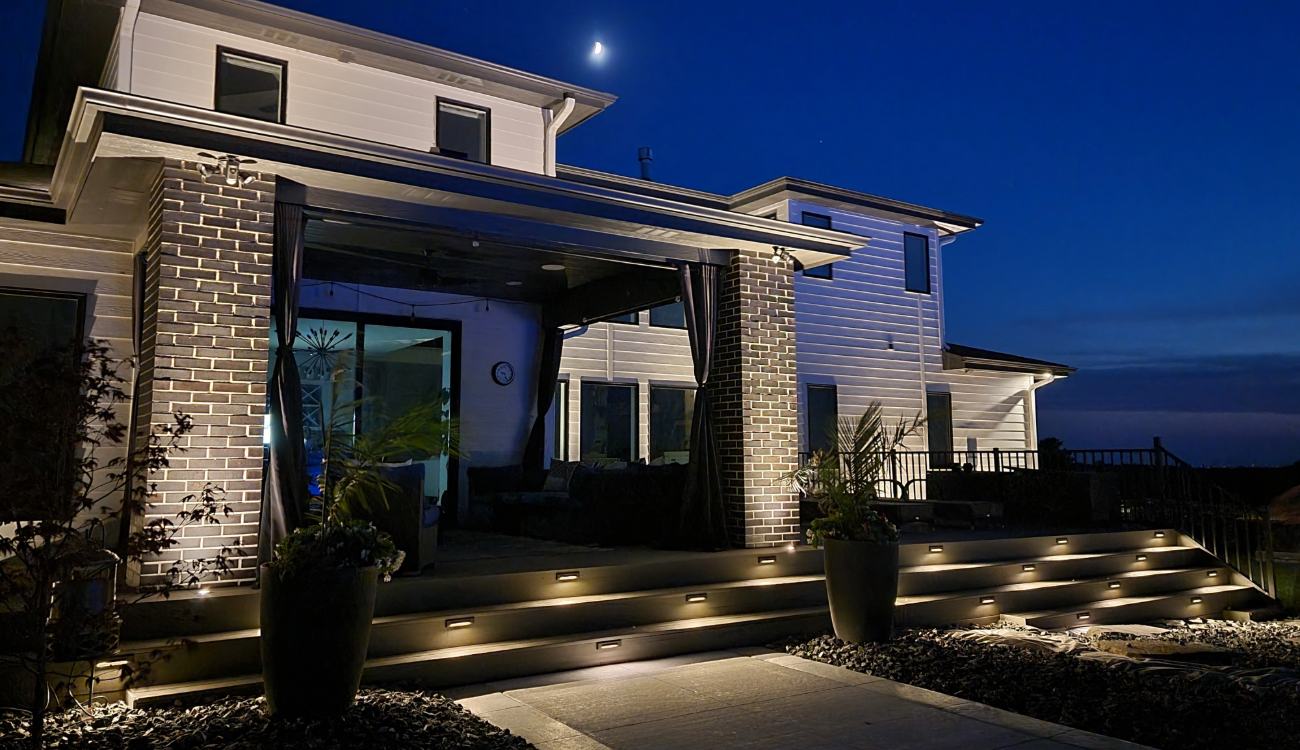 A modern backyard patio with integrated step lights and pillar illumination, showing the services of an outdoor lighting contractor.