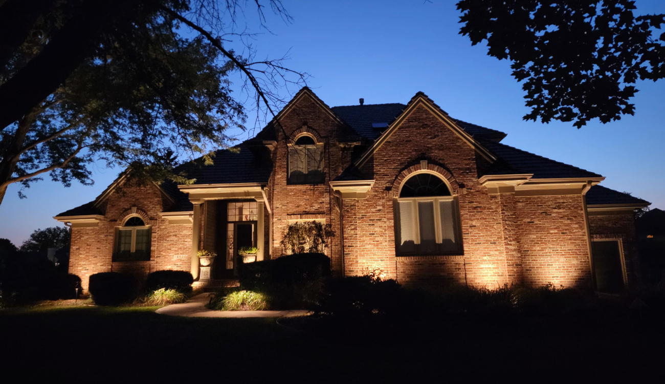 A brick house exterior at twilight showing architectural up-lighting installed by an outdoor lighting contractor.